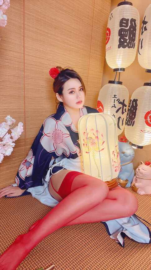 模特水蜜桃米米穿和风浴衣、红色长筒袜，头戴红花，坐在榻榻米上怀抱一个发光的荷花灯笼，背景有招财猫