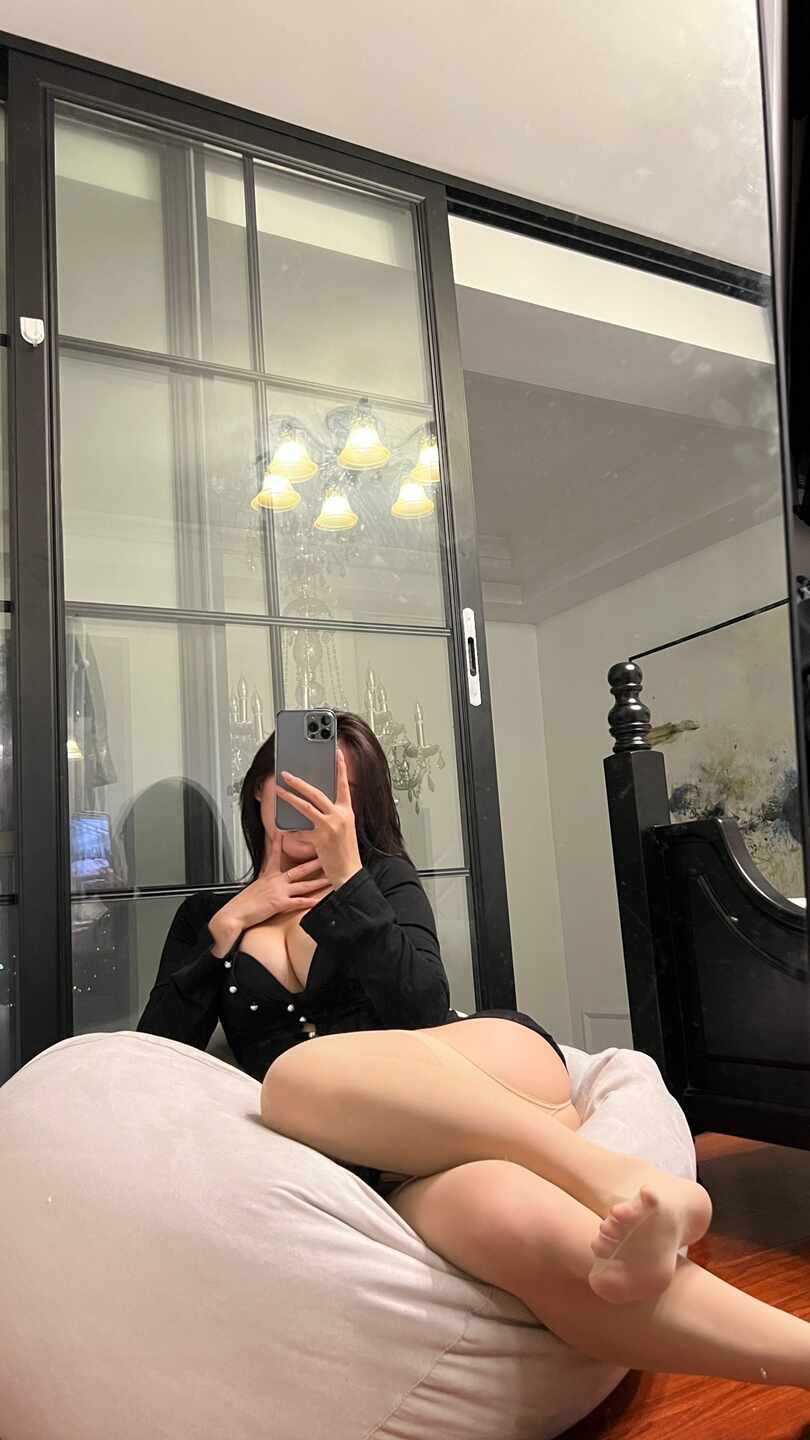 陈大小姐身穿肉色连裤袜和黑色深V上衣，侧躺在米白色懒人沙发上，手持手机遮脸对镜自拍，姿态慵懒。