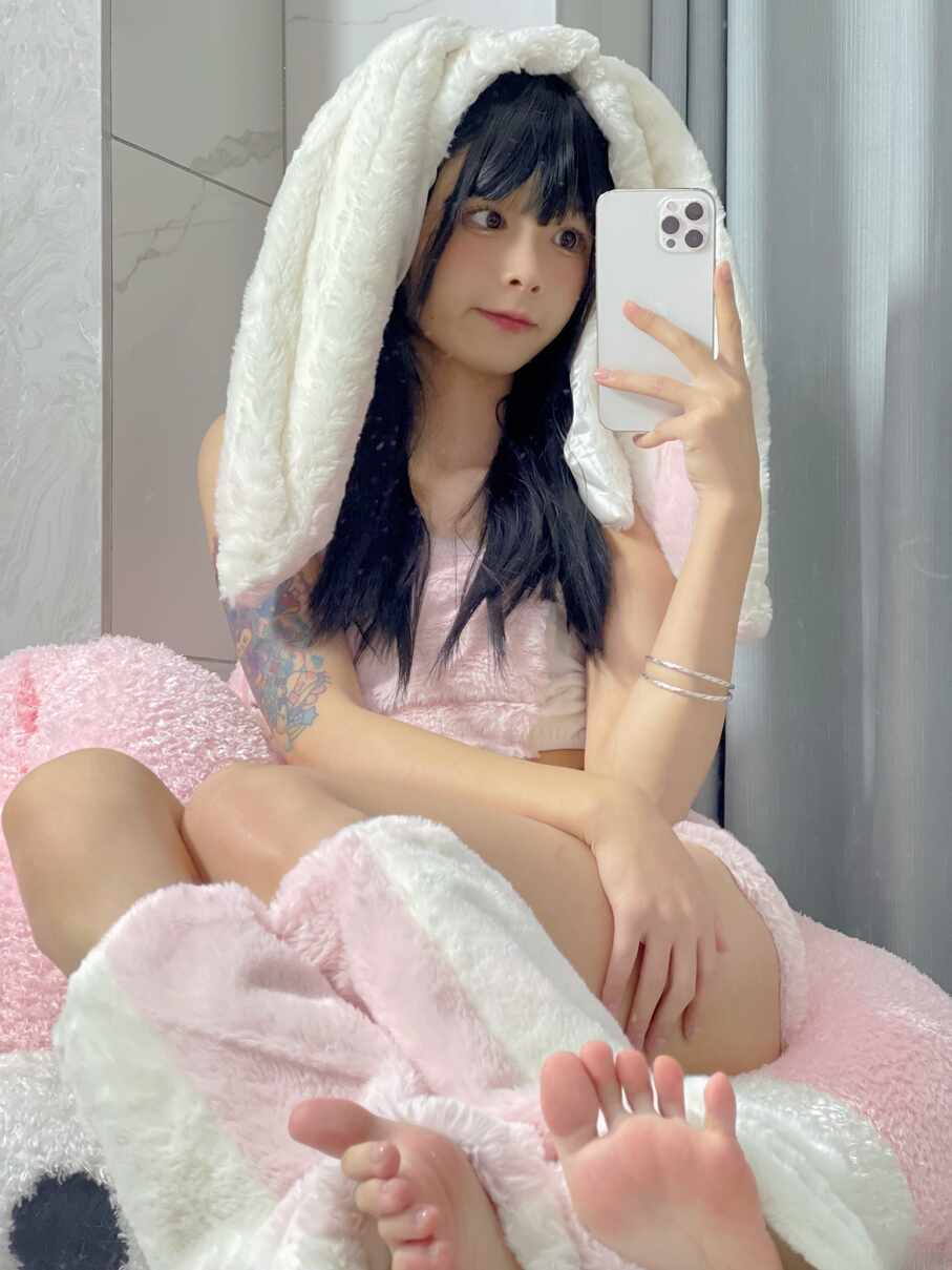 模特聂傲娇戴着绒毛兔耳兜帽，穿着粉色上衣，侧脸望向别处进行自拍，手臂纹身可见