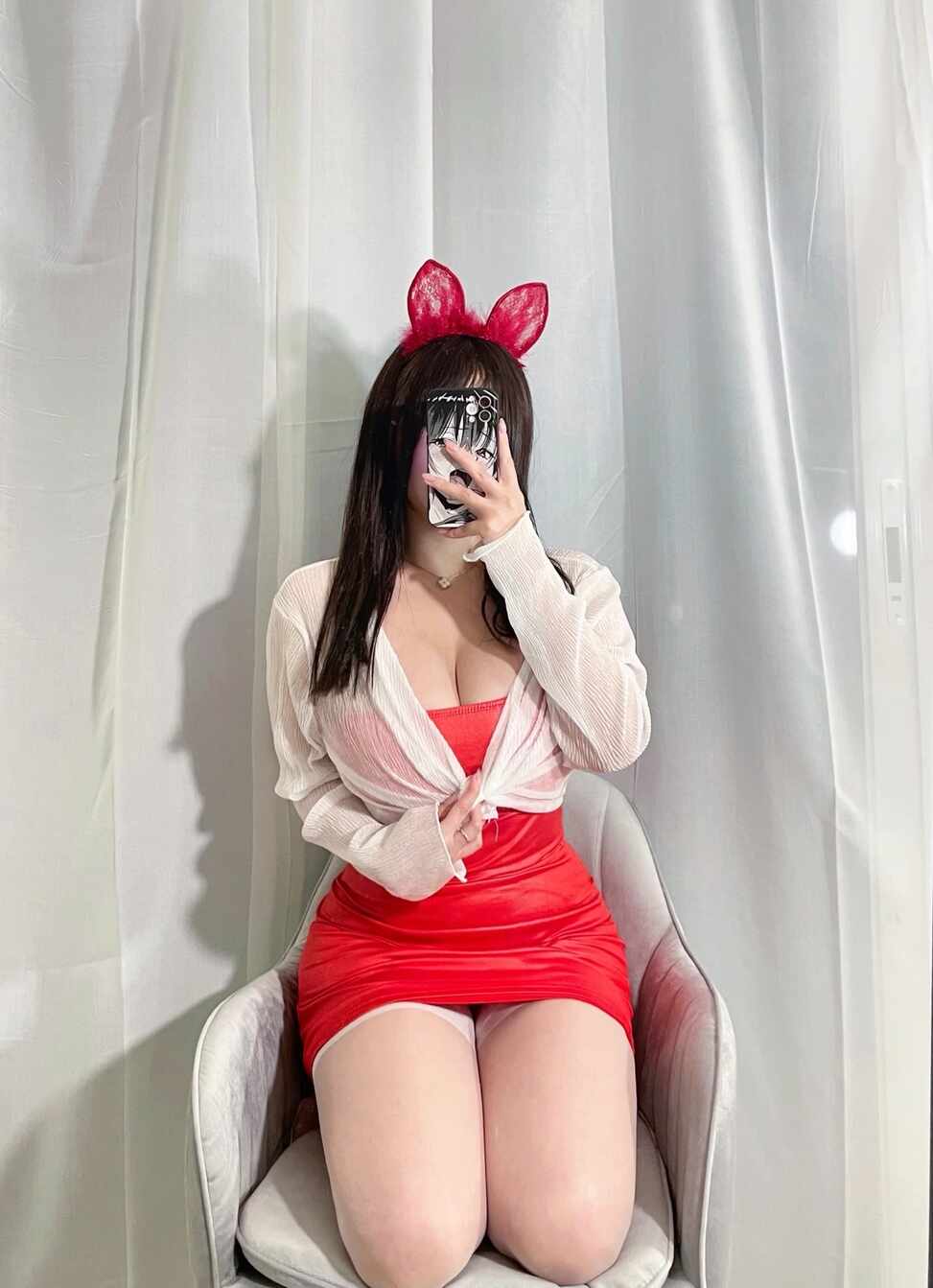 模特是可馨耶穿着红色连衣裙（或上衣）、白色开衫和白丝，戴红色兔耳朵，坐在椅子上自拍