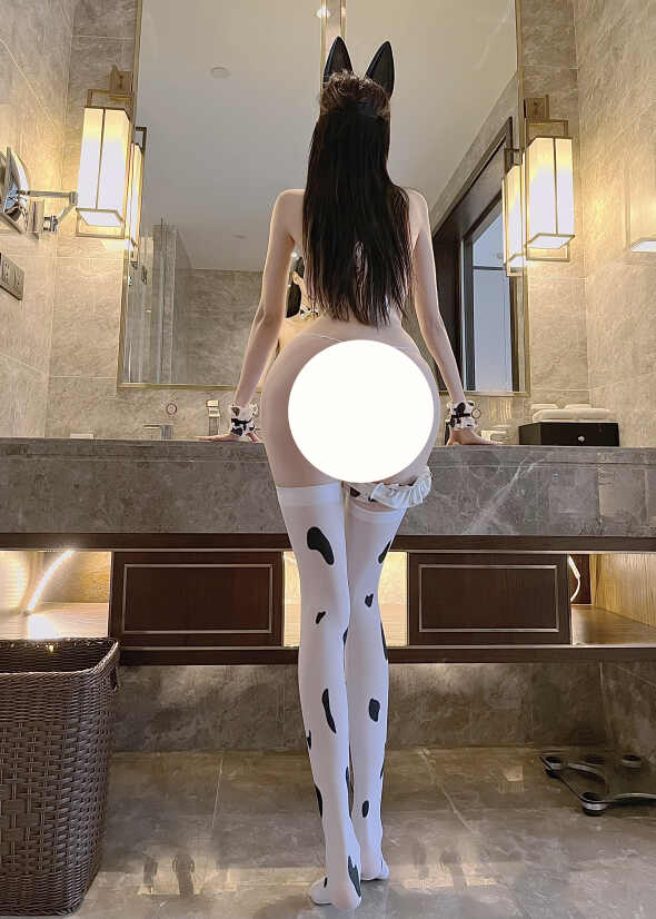 脸红Dearie佩戴黑色兔耳面具，身穿奶牛斑点抹胸和白色黑斑点长筒袜，背对镜头站在浴室洗手台前（臀部区域经白色圆形编辑遮挡）。