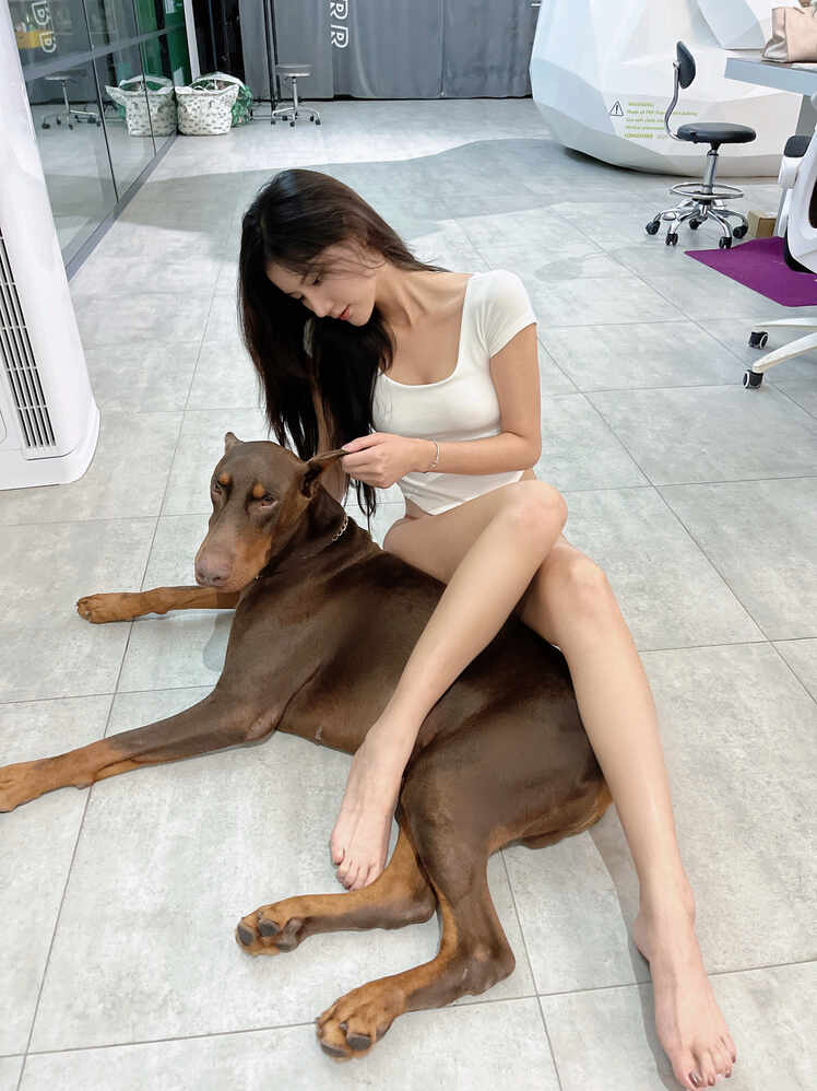 “就是阿朱啊-白T红韵与杜宾萌宠情”嘉宾写真，模特身着白色T恤与简约内裤坐在地板上，杜宾犬温顺地躺在其腿间或身旁，画面温馨。