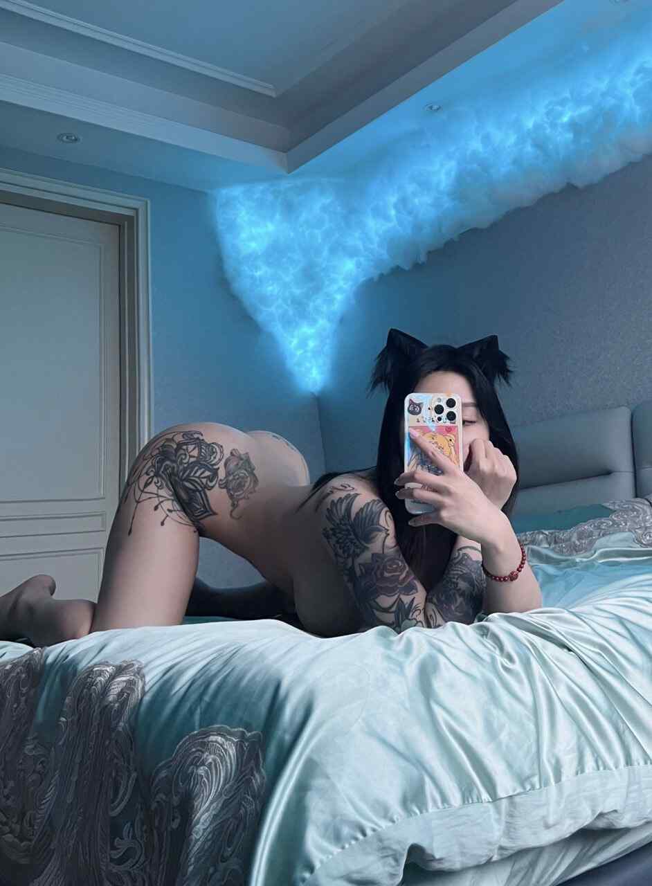宋昱欣佩戴黑色猫耳，在带有蓝色云朵灯饰的床榻上进行艺术自拍，展现“云端猫耳幻想自拍”主题的背部曲线与个性纹身。