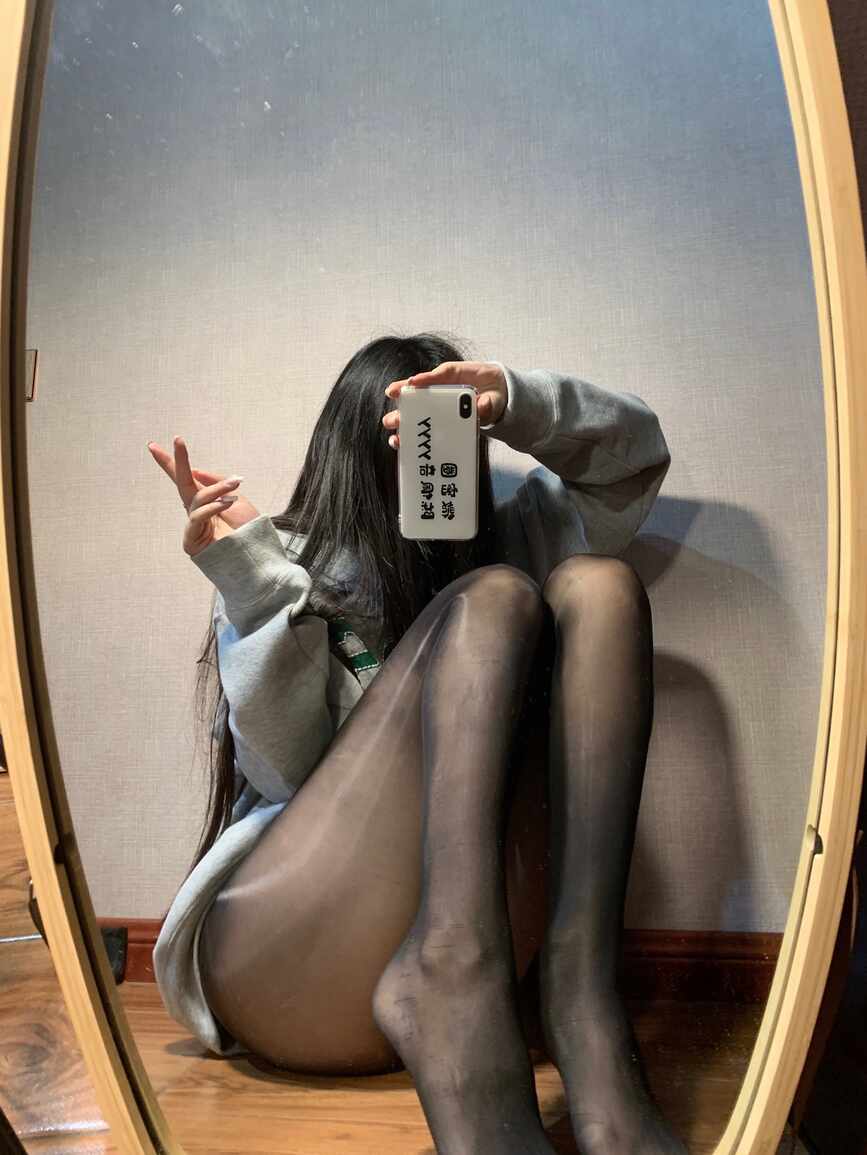 陈佩奇yyyy身着灰色卫衣与黑色光泽感丝袜，慵懒地坐在椭圆形镜子前的木地板上，手比V字进行时尚自拍，展现“黑色光泽袜镜前慵懒自拍”主题。