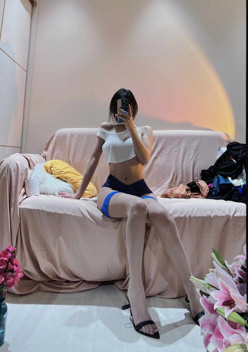 我就是张包包身着白色露脐上衣、蓝色蕾丝底裤与白色丝袜，坐在沙发上进行镜前OOTD自拍，展现“蓝白撞色镜前OOTD”的时尚魅力。