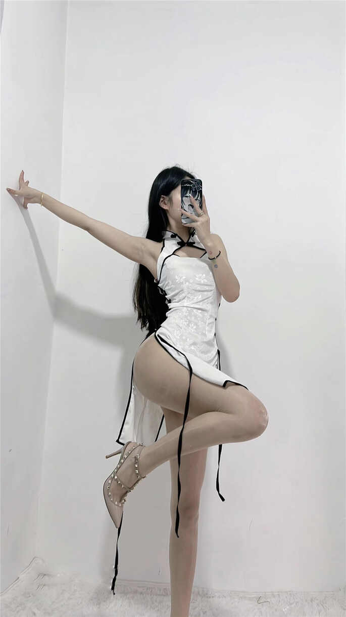 Coser陈佩奇yyyy身穿一件白色暗纹的改良款高开衩旗袍，搭配白色丝袜和铆钉高跟鞋，在白色背景墙前，以一个舒展的姿势用手机对着镜子自拍。